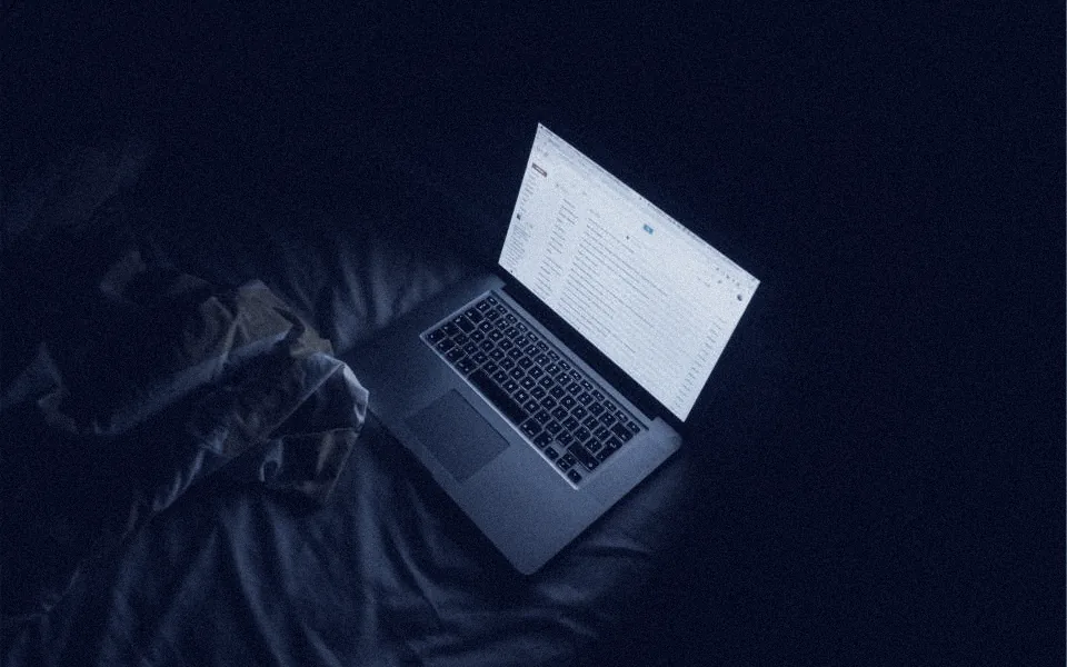Notebook aberto, com a tela acesa, num quarto escuro.